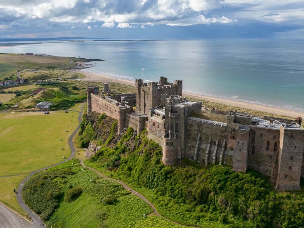 Bamburgh Castle with the beach and coastline behind it on top of a hill