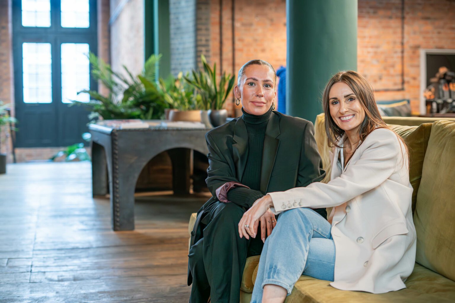 Two businesswomen smile sat on a couch